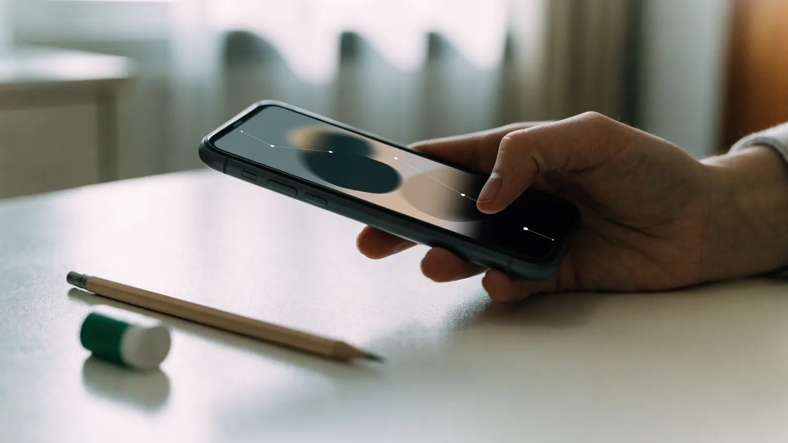 Celular exibindo uma mensagem do WhatsApp sendo corrigida, com lápis e borracha ao lado sobre a mesa